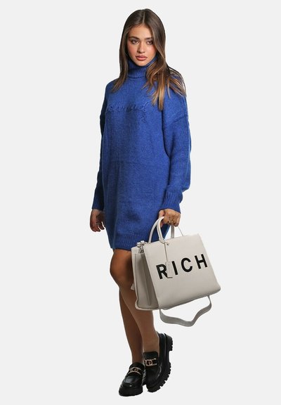 Abito maglione blu con collo alto; mocassini neri chunky; borsa bianca con la scritta 'RICH' stampata in bold nero.