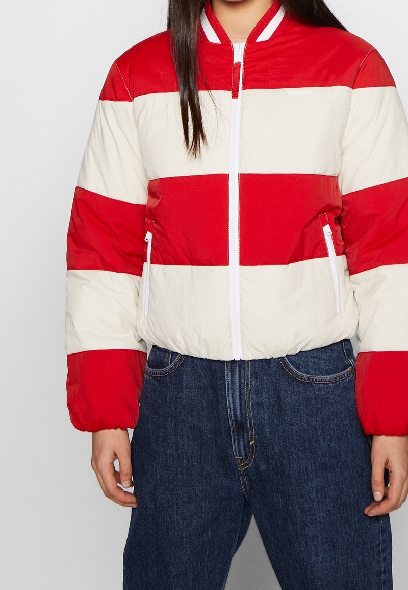 Giacca bomber a righe rosse e crema con zip frontale, polsini elasticizzati e tasche laterali. Tessuto leggero e trapuntato con un design sportivo.