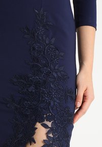 Abito navy con ricami floreali, caratterizzato da dettagli intricati lungo il lato. Il tessuto ha una texture liscia e una fessura all'orlo.