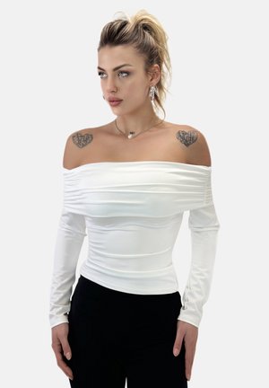 Off-the-shoulder witte top van rekbare stof, met gerimpelde textuur, lange mouwen en een aansluitend ontwerp. G gedragen met zwarte broek.