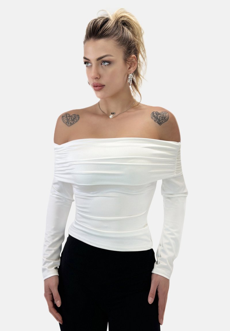 Top bianco scollato sulle spalle realizzato in tessuto elastico, con texture arricciata, maniche lunghe e design aderente. Indossato con pantaloni neri.