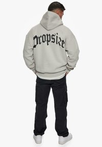 Hooded sweatshirt in light gray with "Dropsize" printed in black on the back, paired with black cargo pants and white sneakers.
