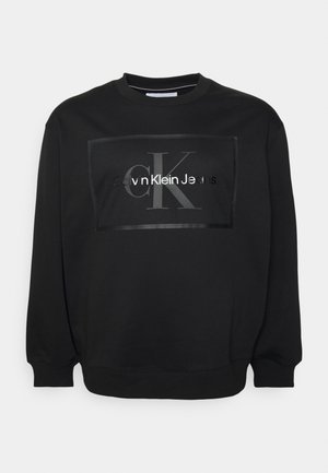 Sudadera negra de tela suave, con un logo rectangular en el frente que dice "Calvin Klein Jeans" y "CK" en acabado brillante.