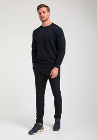 Felpa navy con design testurizzato, scollo rotondo e polsini a coste, abbinata a pantaloni navy slim-fit e sneakers scure con suola chiara.