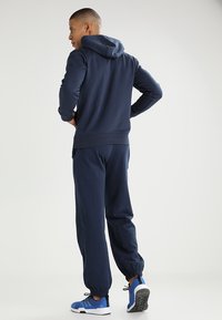 Jūras spēku kapuci ar kangaroo kabatu un aprocēm, apvienots ar saskaņotiem sporta biksēm ar elastīgām potītēm un ziliem sporta apaviem.