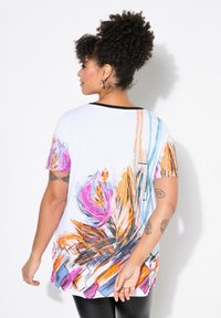 Top blanco de manga corta que presenta un colorido diseño floral en rosa, naranja y azul, con un escote negro y una forma fluida.