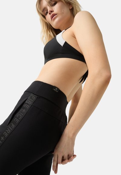 Zwarte sportbeha en bijpassende hoogwaardige legging met een textuur in de tailleband. De legging heeft een verticale logo-detail aan de zijkant.