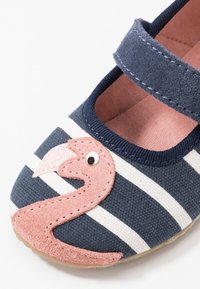 Tossut, joissa on tummansininen ja valkoinen raitakuvio, ja joissa on vaaleanpunainen flamingo-patch varpaassa. Varustettu tarranauhalla ja pehmeällä sisuksella.