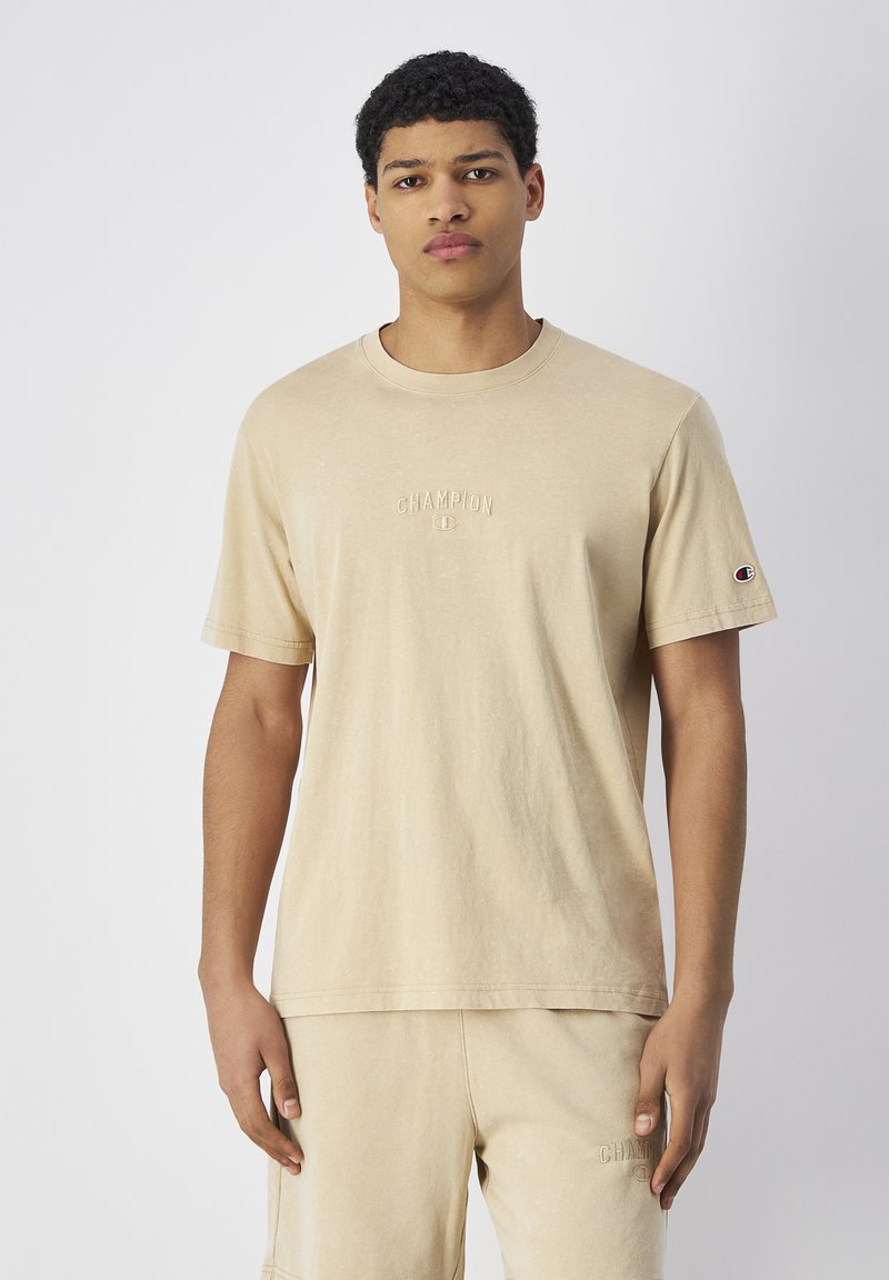 Beige katoenen t-shirt met een klassieke ronde hals, voorzien van een geborduurd "CHAMPION" logo op de borst en een logo patch op de mouw.