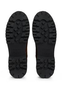 Botas de cuero marrón con suelas de goma negra resistentes que presentan surcos profundos para una mejor tracción. Logo grabado en el lateral de la suela.
