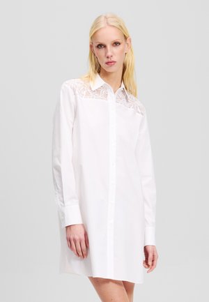 Witte blouse met knoopsluiting en kantdetails op de schouders, lange mouwen en een spitse kraag. Glad katoen, ruime pasvorm, zijsplitten aan de zoom.