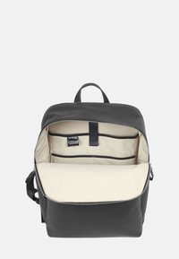 Svart läderryggsäck med dragkedjestängning, beige inredning, inre fickor och handtag ovanför för enkel bärbarhet.