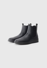Botines negros con un exterior de imitación cuero suave, paneles laterales elásticos y tiradores; suela de goma con una ligera plataforma.
