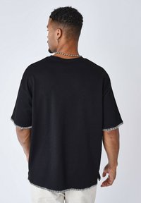 T-shirt nera oversize con maniche corte, texture a coste e cuciture bianche a contrasto lungo le maniche e l'orlo, indossata in modo casual.