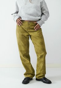 Oliwkowe spodnie kordorowe o prostym kroju, z zapięciem na guzik z przodu i paskami do pasa. W połączeniu z czarnymi loafersami.