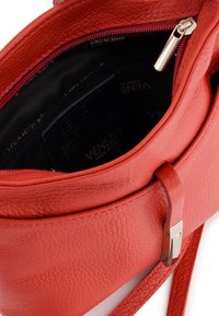 Red leather handbag with a textured finish. Features a zippered closure and a smooth strap. Interior lined with black fabric marked "VENEZIA."