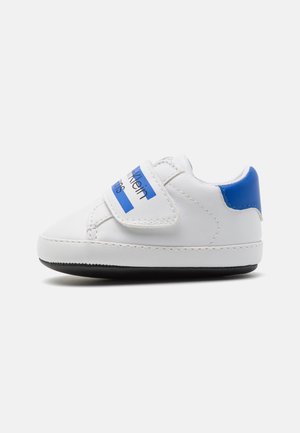 Hvid baby-sneaker med blåt hælpanel, sort sål og velcrolukning med blå striber og sort tekst.