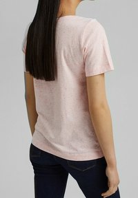 Camiseta rosa de manga corta con un patrón moteado, textura suave y un ajuste clásico, combinada con jeans azul oscuro.