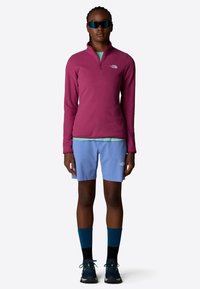 Sudadera de forro polar en rosa bayas con cremallera hasta la cuarta parte, combinada con pantalones cortos azul claro, calcetines azul marino y zapatillas oscuras, acentuada con un logotipo.