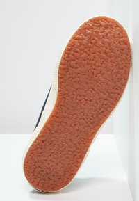 Gummi såle med en teksturert oransje overflate, kantet med en hvit kant og med en marineblå øvre del. Merket med "SUPERGA."