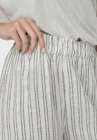Pantaloni in misto lino con vestibilità rilassata. Presentano un cinturino arricciato, righe verticali bianche e marroni, e una texture leggera.