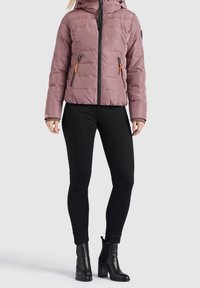 Rosa puffjacka med horisontella sömmar, framdragkedja, två fack med dragkedja och huva; kombinerad med svarta åtsittande byxor och klackade ankelstövlar.