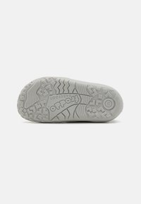 Semelle de chaussure en caoutchouc gris avec des motifs de bande de roulement texturés pour une adhérence, détail de logo circulaire et numéro de taille embossé sur le talon.