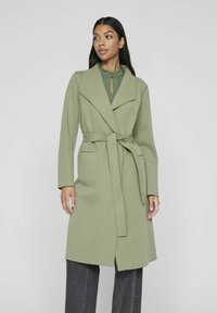 Olive green, long coat in soft fabric with a wrap design, large lapels, and a tied waist belt. Features two front pockets and full sleeves.