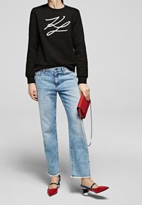 Sudadera negra con logo blanco, vaqueros de pierna recta azul claro, bolso rojo con cadena y zapatos de tacón rojo con detalles en azul y puntera afilada.