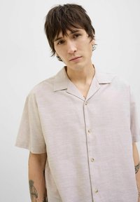 Chemise rose clair à manches courtes, à boutons, avec une coupe décontractée. Elle présente un col de type camp et une texture subtile, rehaussée de boutons marron clair.