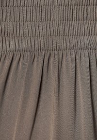 Brązowa, strukturalna tkanina z serią elastycznych, marszczonych fałd. Materiał jest gładki z delikatnym połyskiem.