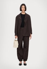 Veste oversize marron à rayures avec pantalon assorti, associée à un haut noir et un sac à main blanc, offrant une silhouette décontractée et des poignets élastiques.