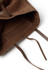 Borsa in suede marrone con una texture morbida, chiusura con cordoncino e spalline sottili. L'interno presenta una fodera liscia e un logo impresso discreto.