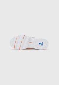 Semelle de sneaker blanche avec des accents orange et bleu, présentant le logo New Balance et un motif de semelle sur un fond uni.