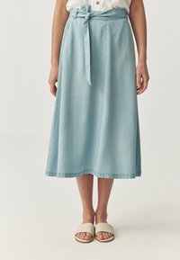 Světle modrá midi sukně vyrobená z denimu s detailem na zavazování v pase. Má čistý design a jemnou texturu, sahá pod kolena.