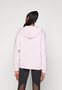 Růžová mikina s kapucí, volného střihu a texturovaným povrchem. Obsahuje velkou kapuci a ribbované manžety, doplněná černými legínami.