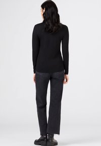 Un haut noir à manches longues associé à un jean en denim sombre à taille haute. Le jean présente un ourlet effiloché et est légèrement ample autour des jambes.