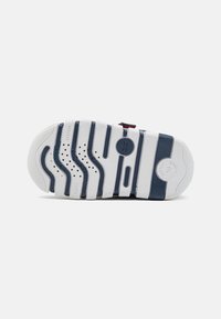 Sole di sneaker bianca con accenti blu navy e grigi, caratterizzata da un motivo a onda, fori di ventilazione e markings che indicano marca e modello.