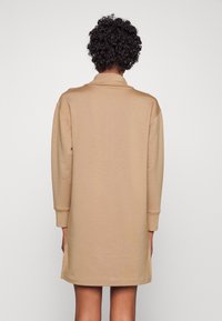 Beiges Sweatshirtkleid mit langen Ärmeln, Kragen und seitlichen Schlitzen, aus weichem Stoff gefertigt. Einfacher, lässiger Schnitt, der bis zur Mitte des Oberschenkels reicht.