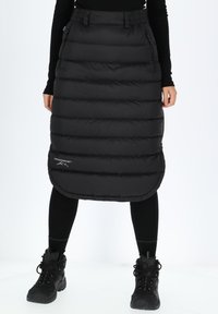 Black puffy skirt with quilted design, elastic waistband, and side pockets, worn over black leggings and sturdy black boots.