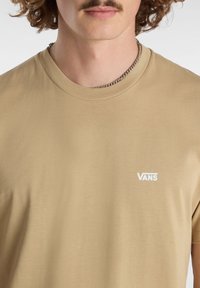 Béžové bavlněné tričko s kulatým výstřihem a krátkými rukávy. Na levé části hrudi má malé bílé logo Vans. Hladká textura.