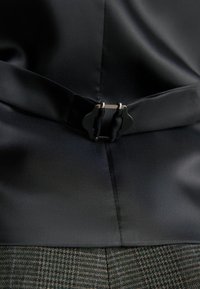 Un tissu en satin noir avec une texture lisse présente une boucle en métal argenté à la taille, associé à une partie inférieure à motif plaid.