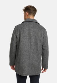 Cappotto in lana grigia con colletto a puntale, forma strutturata e dettagli di cucitura visibili. Presenta maniche lunghe e un design di lunghezza media.