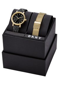 Sada hodinek DKNY obsahuje hodinky s černým vzorovaným silikonovým páskem a zlatým síťovým páskem, které jsou vystaveny v černé krabičce s bílým logem DKNY.