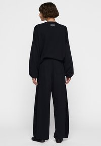 Zwarte oversized sweatshirt met verlaagde schouders en een label op de rug, gecombineerd met wijde zwarte broek met een achterzak.