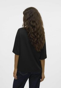 Camiseta negra de gran tamaño con mangas cortas y un corte relajado, que presenta una tela texturizada. Combinada con jeans oscuros, mostrando un diseño simple.
