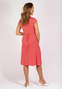 Rotes Polka-Dot-Kleid mit kurzen Ärmeln, schwingendem Rock und einer Bindeschleife am Rücken. Glatte Textur und knielanges Design.