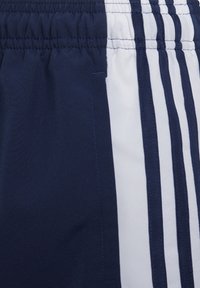 Marineblaue und weiße Sportshorts mit marineblauem elastischem Bund, Seitentasche und drei vertikalen marineblauen Streifen auf dem weißen Bereich.