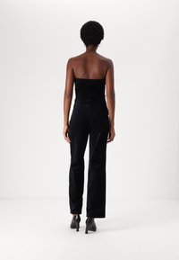 Svart sammetslinne utan axelband, kombinerat med högmidjade svarta byxor med en slät yta och en något lös passform. Svarta klackar fulländar stilen.