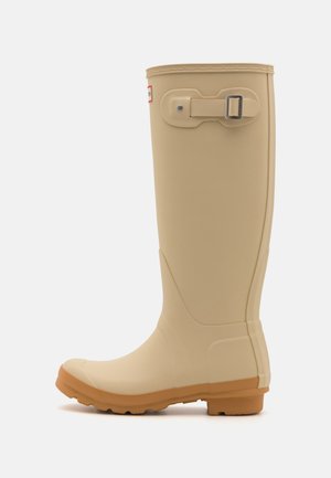 Beige rubber laarzen tot de knie voor regen met een gestructureerde bovenkant, een stevige zool en een gespsluiting bij de bovenkant. Voorzien van een ronde neus en een stevige profielzool.
